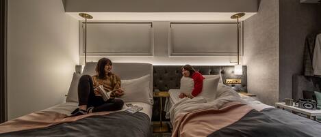 A hotel room with two beds, a ceiling projector, and a small table with a cup and a radio.