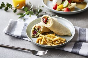 A plate with a wrap, fries, and a glass of orange juice on a table with a striped napkin. - slash kawasaki (Kawasaki)