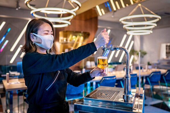 Une personne servant une boisson à partir d’un robinet dans un bar moderne, avec des luminaires au design contemporain.
