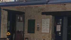 Una stanza con parete in pietra rustica, una porta in legno e una finestra decorata con girasoli. Si vede una sedia bianca e un tavolo con tovaglia bianca.
