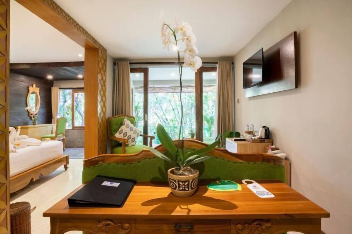 A hotel room with a wooden desk, a potted orchid, a green sofa, a bed, and a TV mounted on the wall.