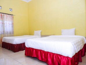 A hotel room with two beds, each with white bedding and red skirts. The walls are yellow, and there is a window with a curtain.