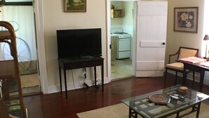A living room with a television, a glass coffee table, a sofa, a wooden chair, and a ceiling fan. - 2 Melinda’s Garden Apt  (Natchez)