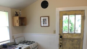 A kitchen with a gas stove, a sink, a wooden cabinet, a framed picture on the wall, and a door with a window. - 2 Melinda’s Garden Apt  (Natchez)