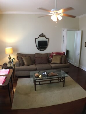 A living room with a ceiling fan, a sofa, a glass coffee table, and a lamp. - 2 Melinda’s Garden Apt  (Natchez)