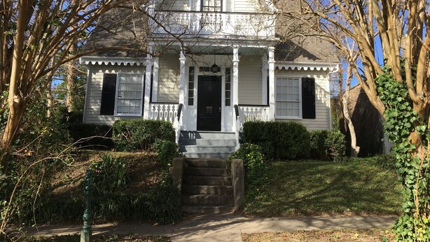A white house with a front porch, a black door, and a small staircase leading up to the entrance. - 2 Melinda’s Garden Apt  (Natchez)