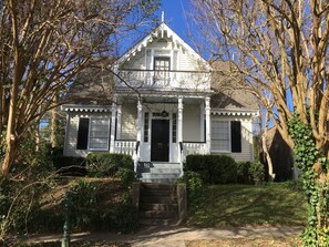 A white house with a front porch, a black door, and a small staircase leading up to the entrance. - 2 Melinda’s Garden Apt  (Natchez)