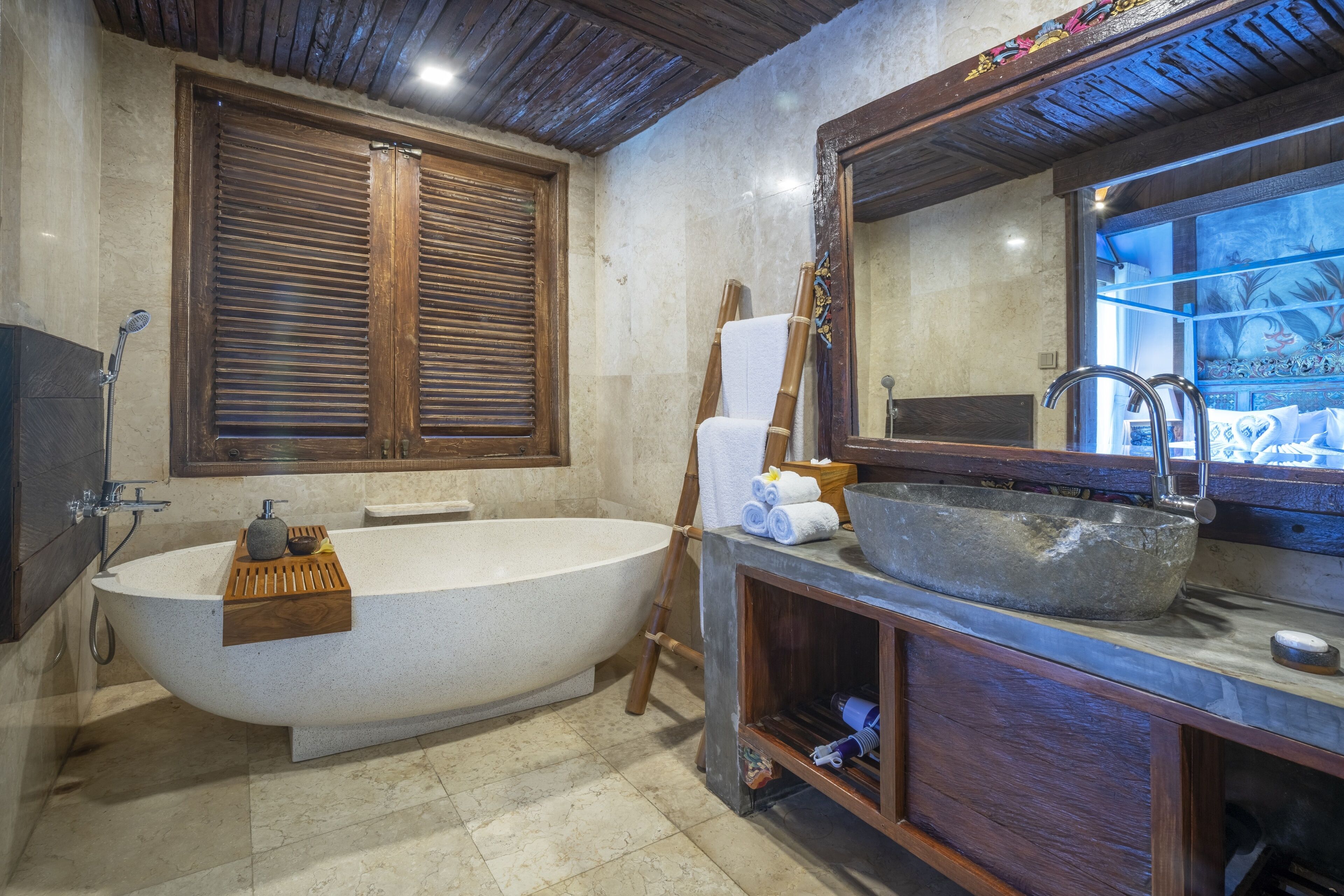 Un baño con una bañera independiente, un espejo grande y un tocador de madera con lavabo de piedra.