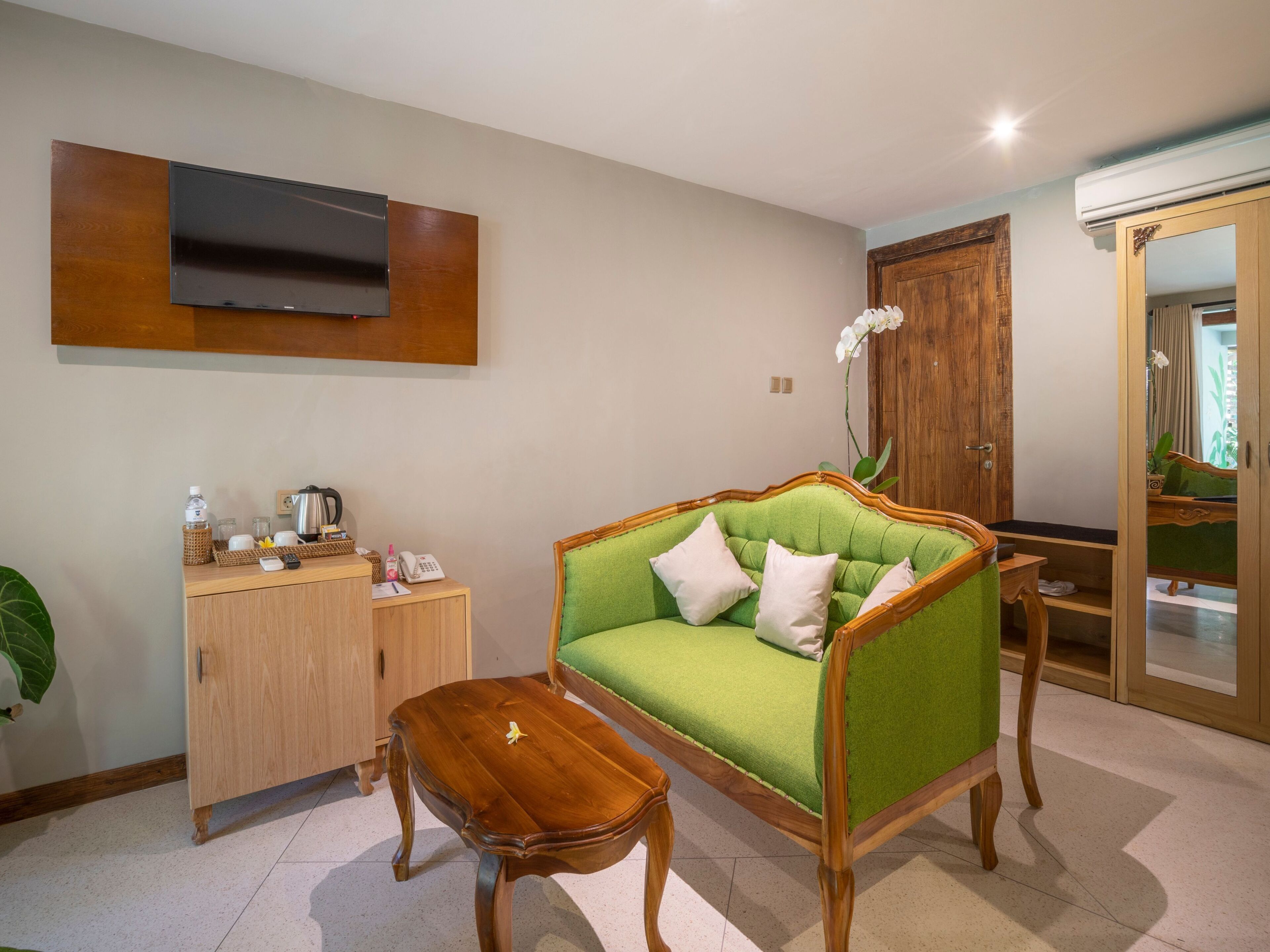 A living room with a green sofa, wooden side table, and a TV mounted on the wall.