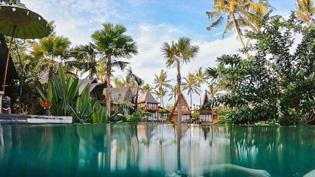 Une piscine aux eaux cristallines où se reflètent les palmiers et des bâtiments de style traditionnel.
