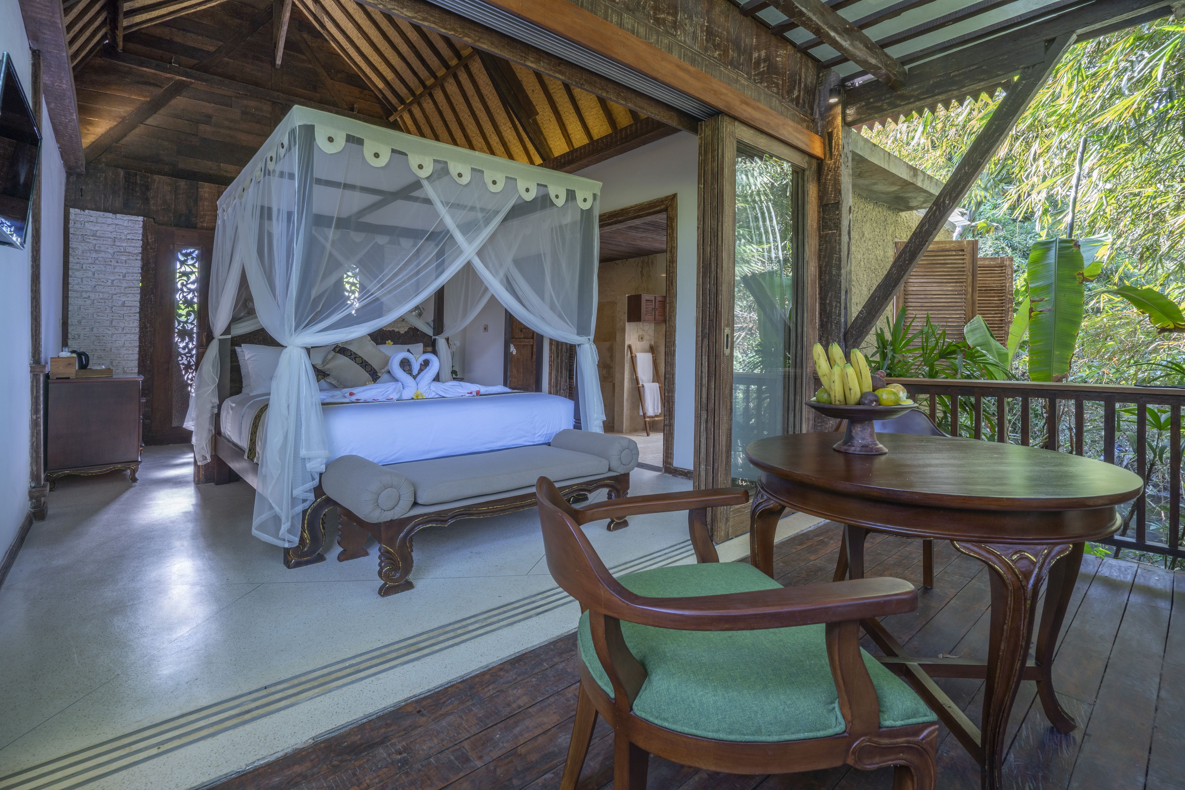 A bedroom with a four-poster bed, a wooden chair, and a table with a banana bowl.