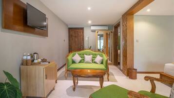 A spacious room with a green sofa, wooden furniture, a TV mounted on the wall, and a large mirror.