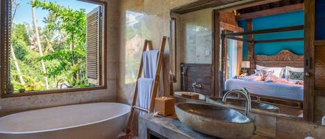 A bathroom with a freestanding bathtub, a large mirror, and a view of a bedroom.