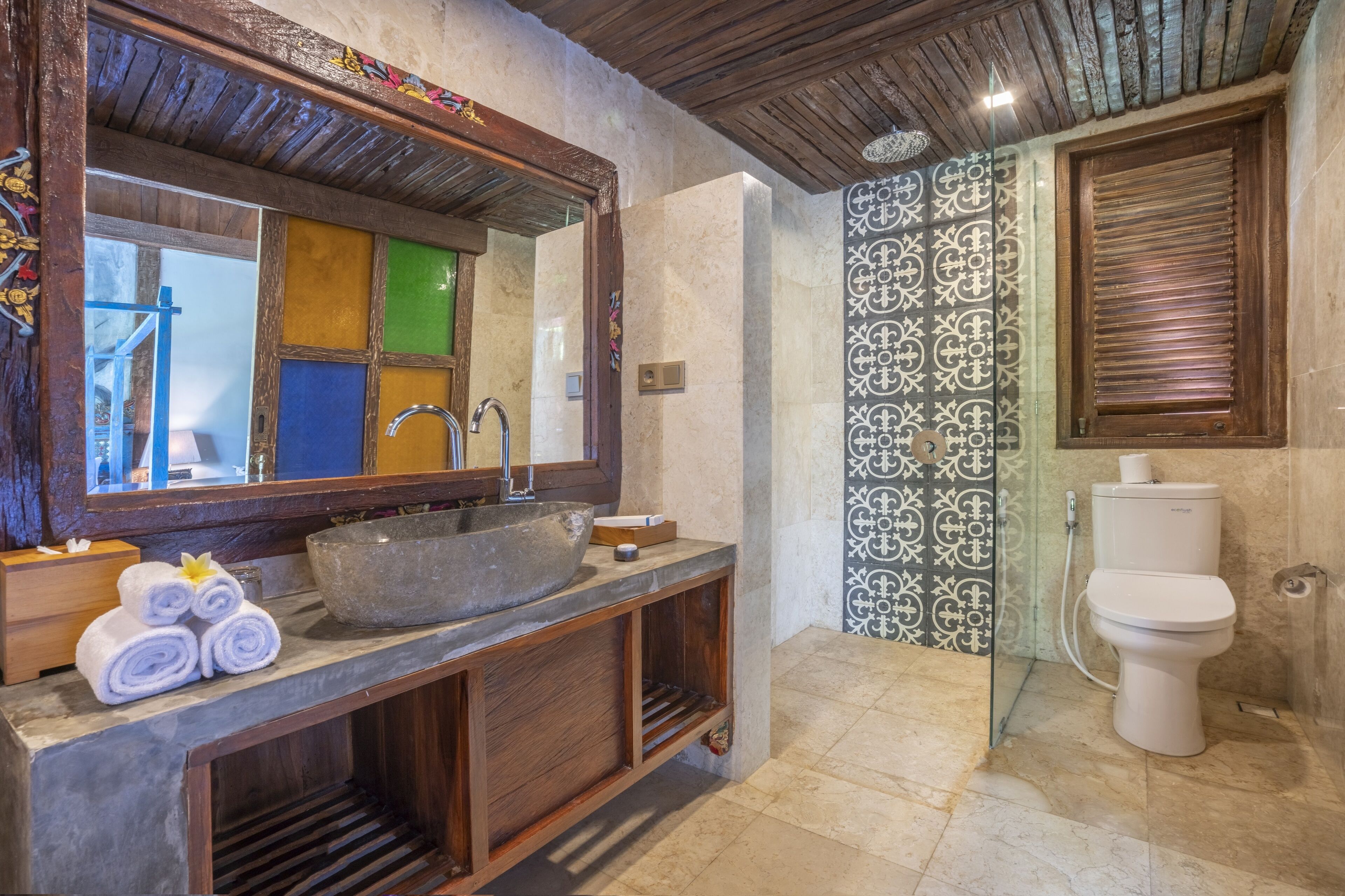 A bathroom with a large mirror, wooden vanity, stone sink, and a toilet.
