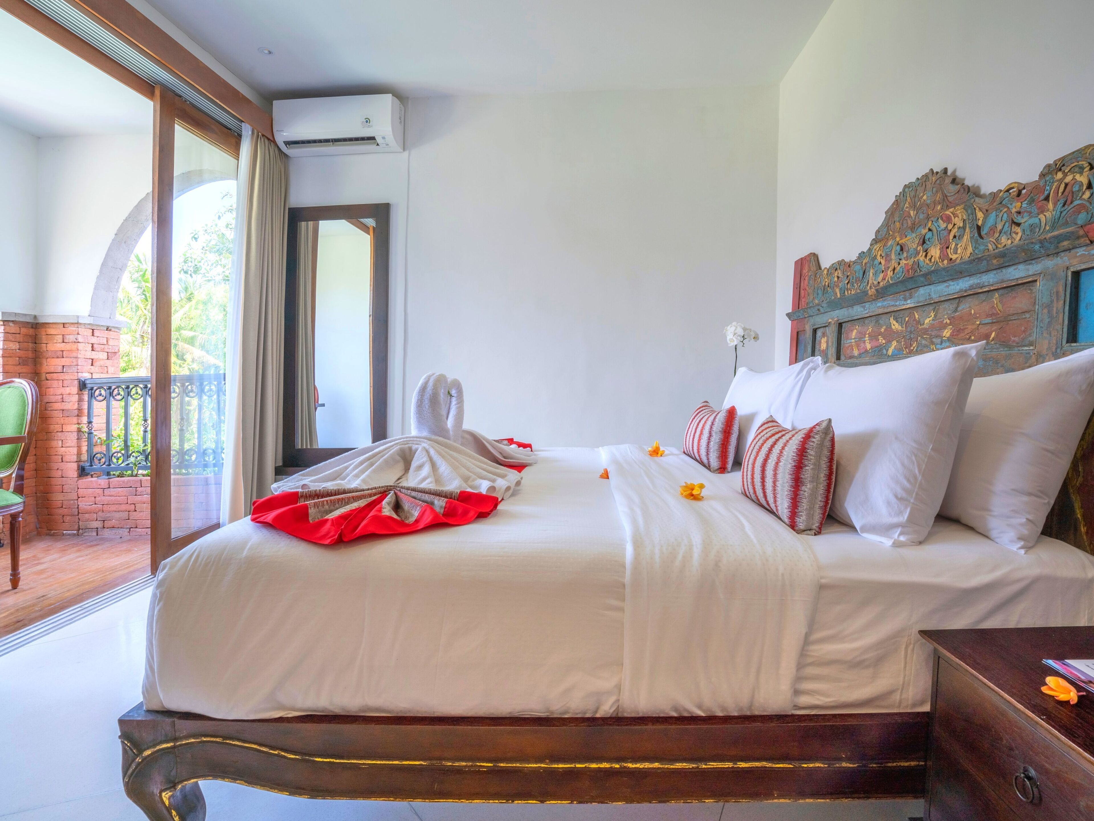 Habitación de hotel con una cama grande, cabecera de madera y balcón con vistas a zonas verdes.