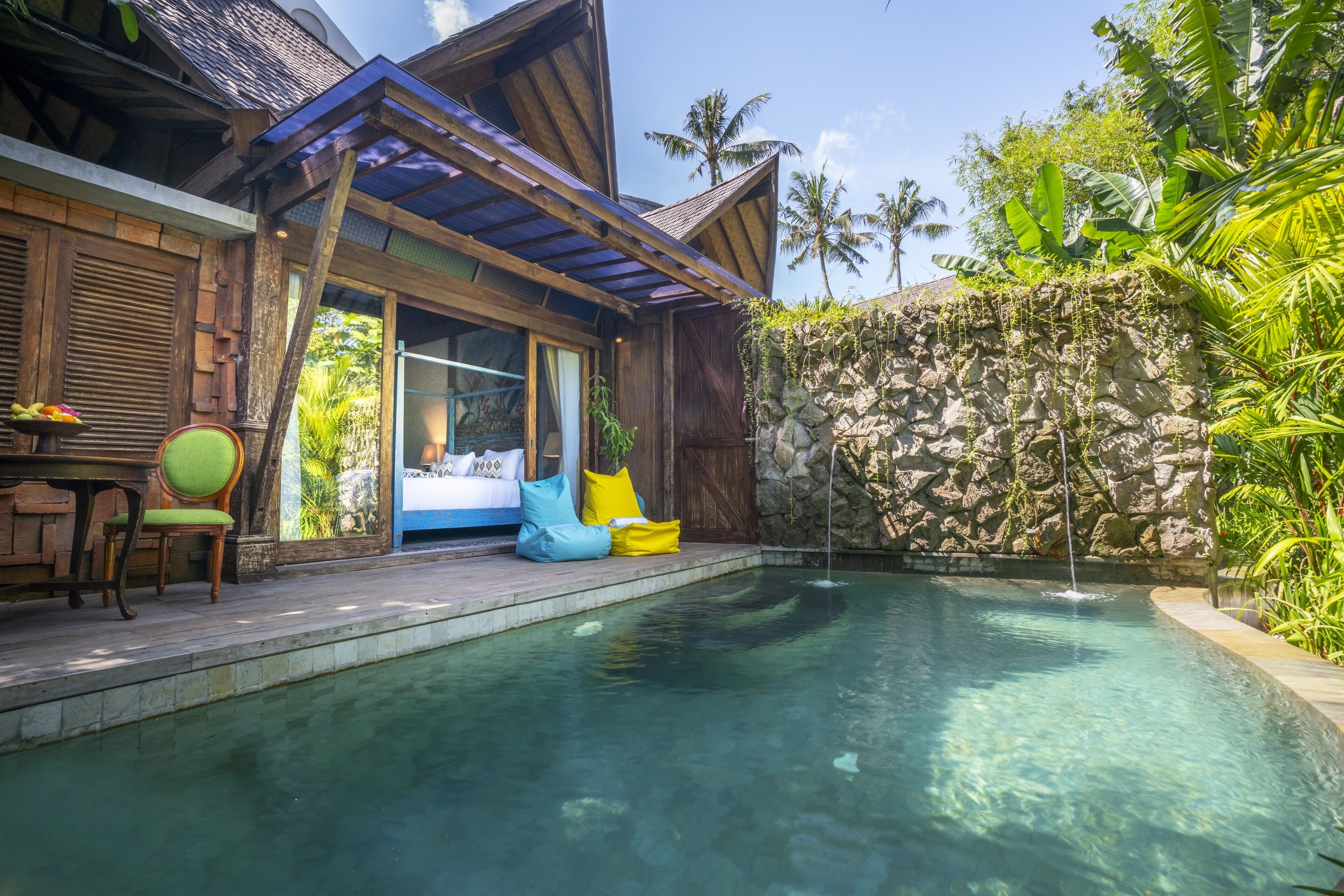 A pool area with a stone wall, wooden deck, and a small waterfall feature.