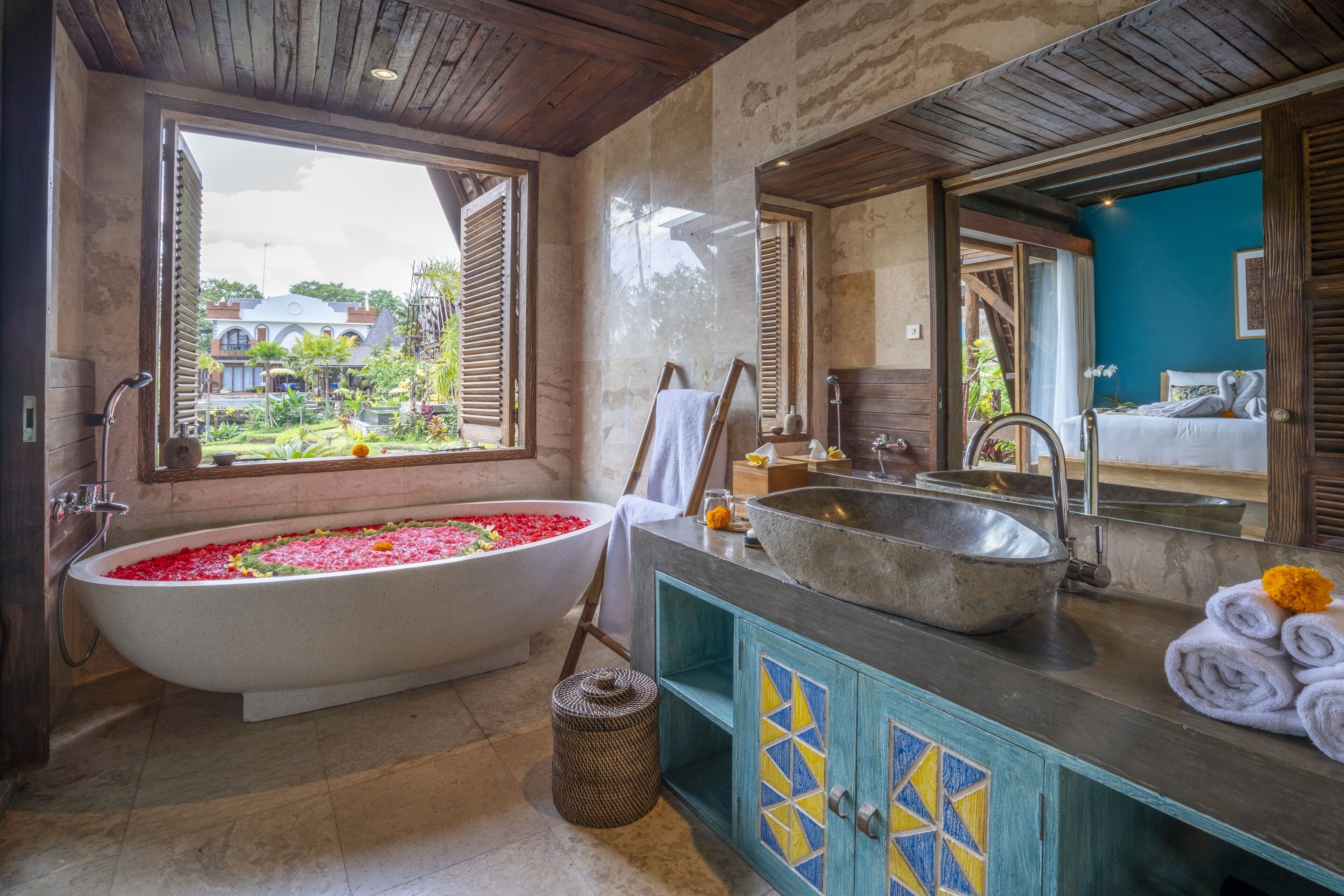 A bathroom with a freestanding bathtub filled with red flowers, a large sink, and a mirror above the sink.