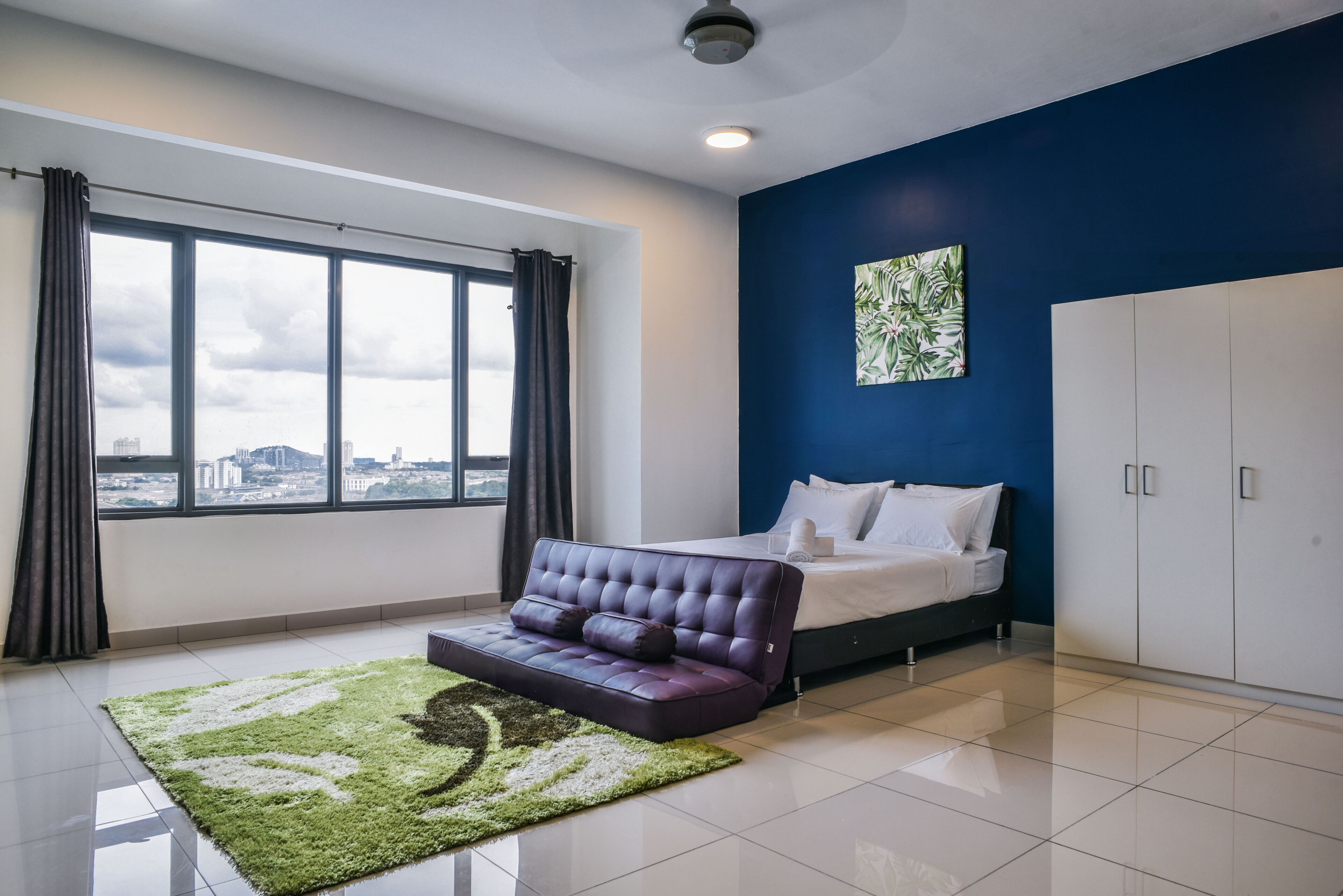 A modern bedroom with a large window, a sofa, a bed, and a wardrobe.