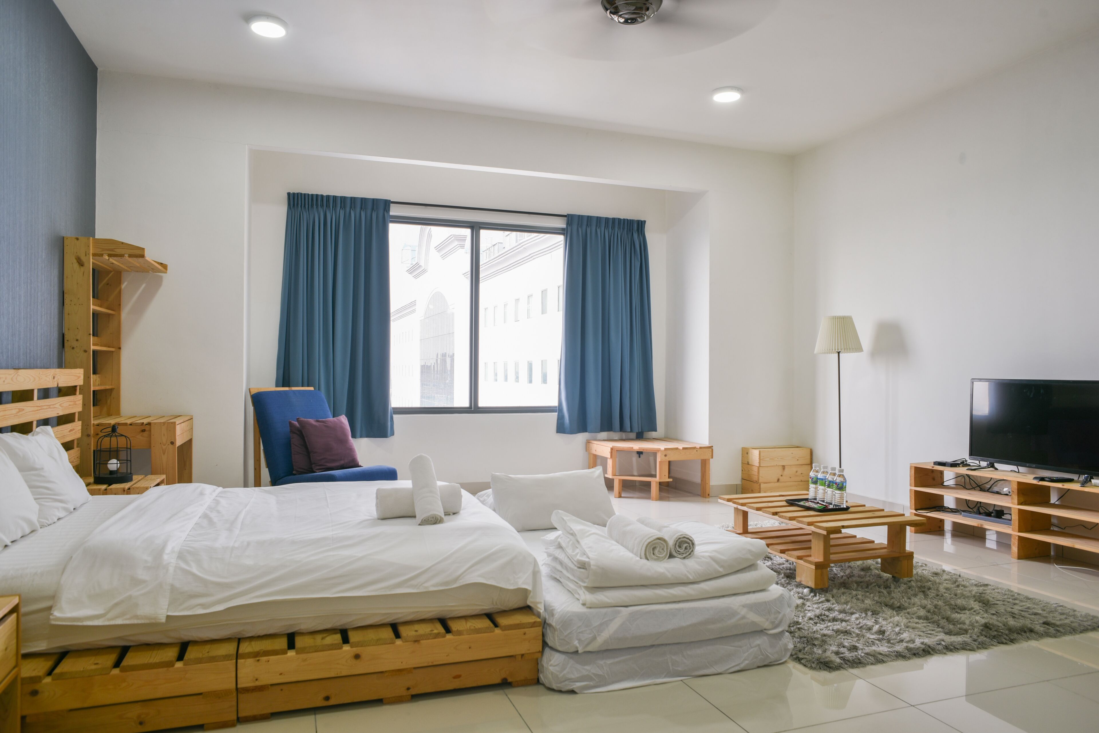 Una habitación de hotel moderna con cama de madera, escritorio, silla, televisor y un gran ventanal con cortinas.