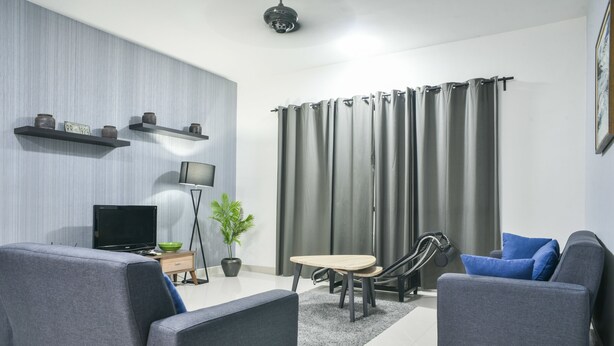 A modern living room with grey sofas, a flat-screen TV, a small table, and a potted plant. - Damen Homestay (Subang Jaya)