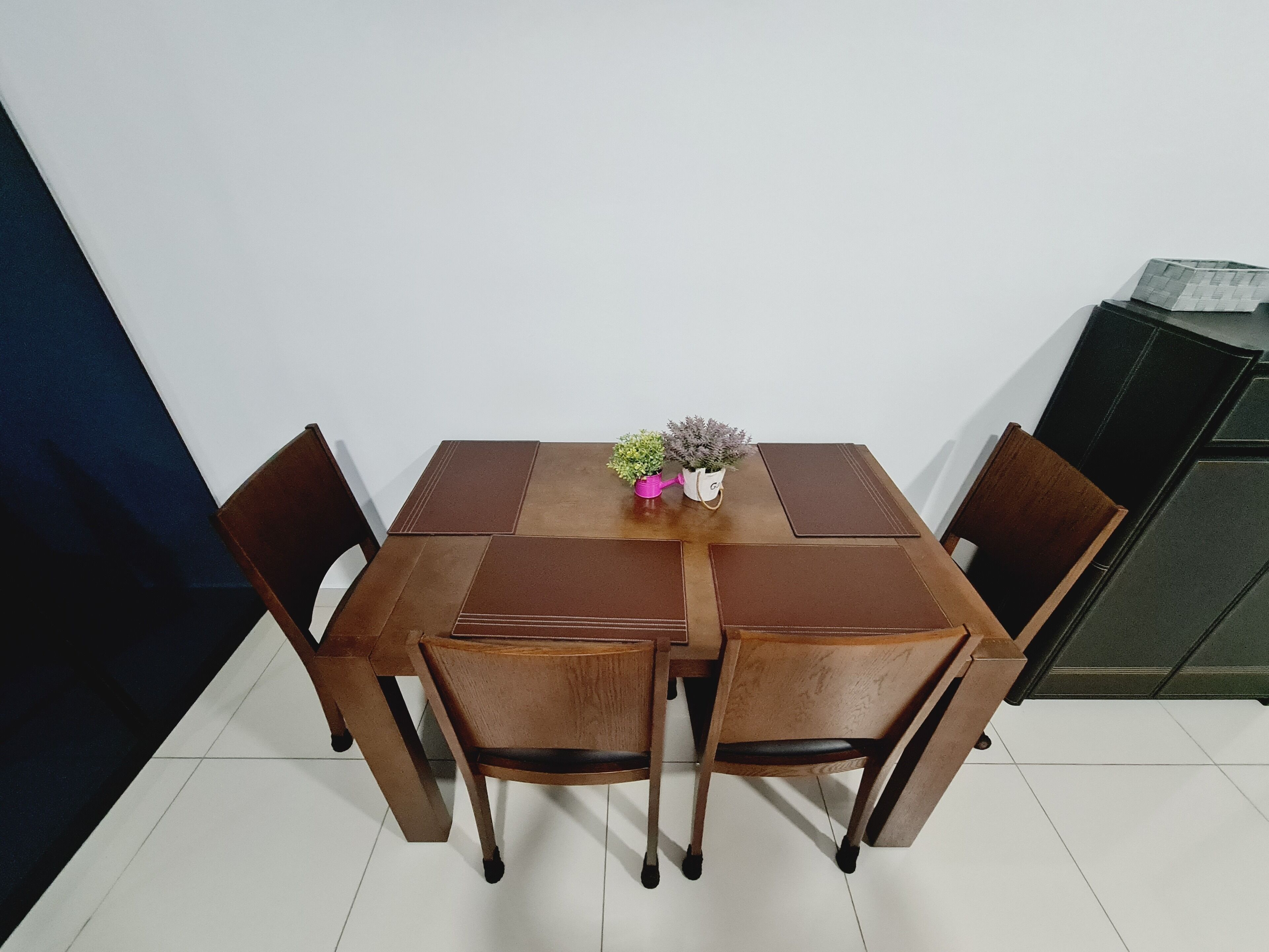 Una mesa de comedor con cuatro sillas, un florero con flores y un aparador al fondo.