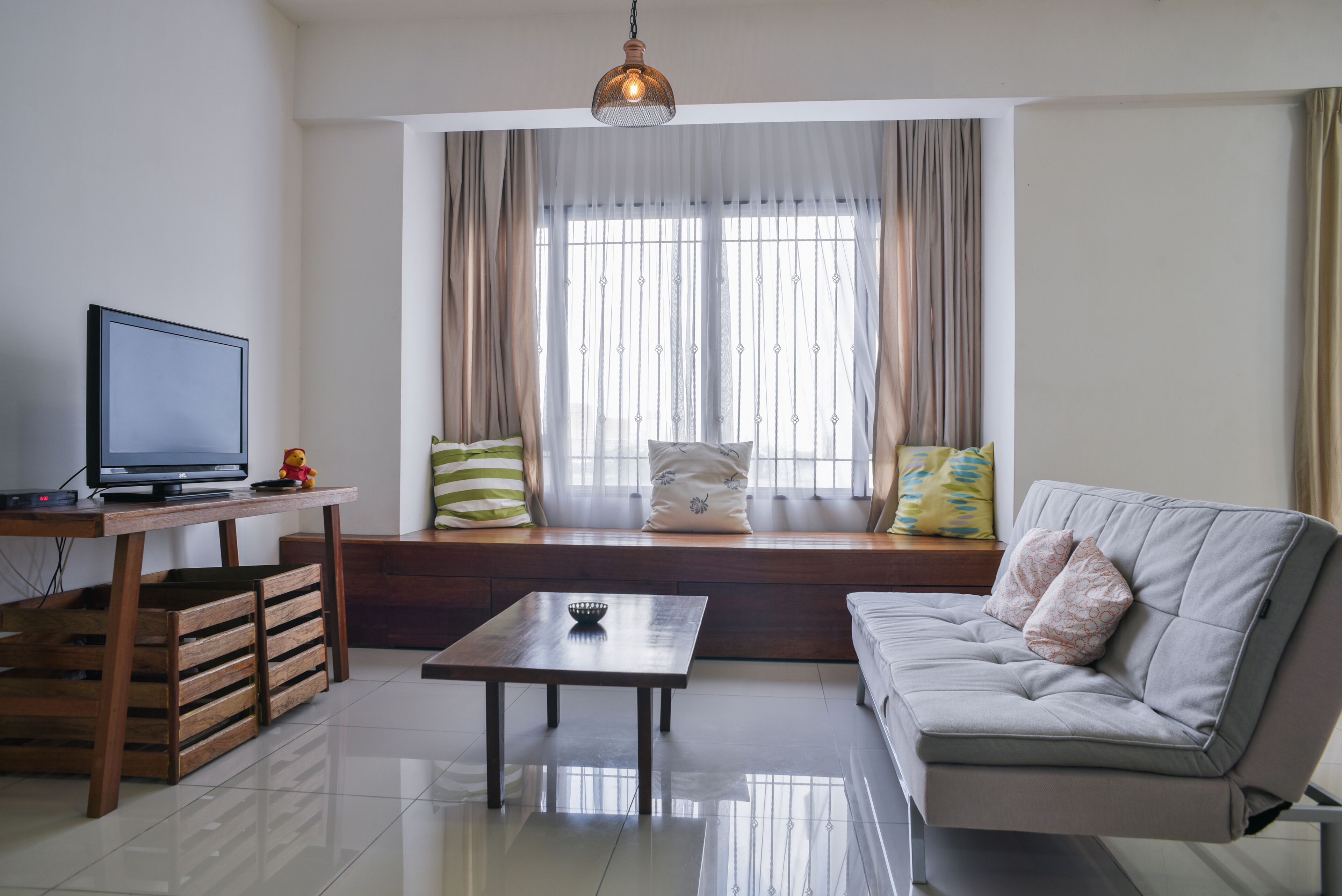 A living room with a sofa, a coffee table, a TV on a wooden stand, and a window with curtains.