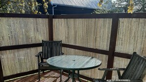 A wooden deck with a round table and two chairs, surrounded by a bamboo fence. - Te Whare Rural Retreat and Caravan (Havelock North)