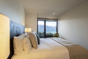 Une chambre d’hôtel moderne avec un grand lit, une vue sur les montagnes et un fauteuil près de la fenêtre.