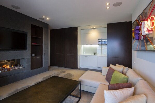 A modern living room with a fireplace, a sofa, and a kitchen area in the background.