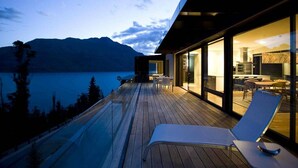 A modern house with a wooden deck overlooking a lake and mountains.