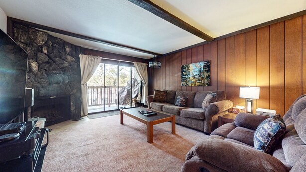 A cozy living room with a stone wall, wooden paneling, a fireplace, a sofa, a coffee table, and a TV.