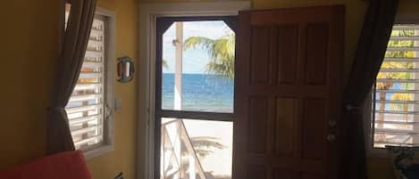 A room with a view of the ocean through a door, a red sofa, and a small table.