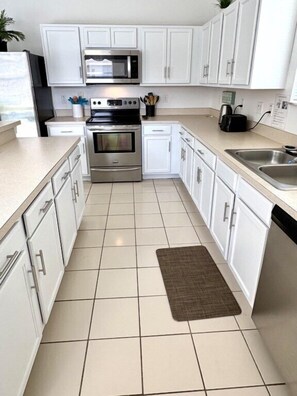 Una cocina con gabinetes blancos, electrodomésticos de acero inoxidable y piso de baldosas.