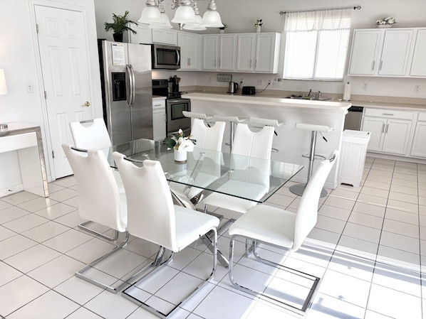A modern kitchen with white cabinetry, stainless steel appliances, and a glass dining table with white chairs.