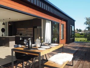 An outdoor dining area with a wooden table, black chairs, and a white fur throw. - Pinot Longbox - Martinborough Holiday Home (Martinborough)
