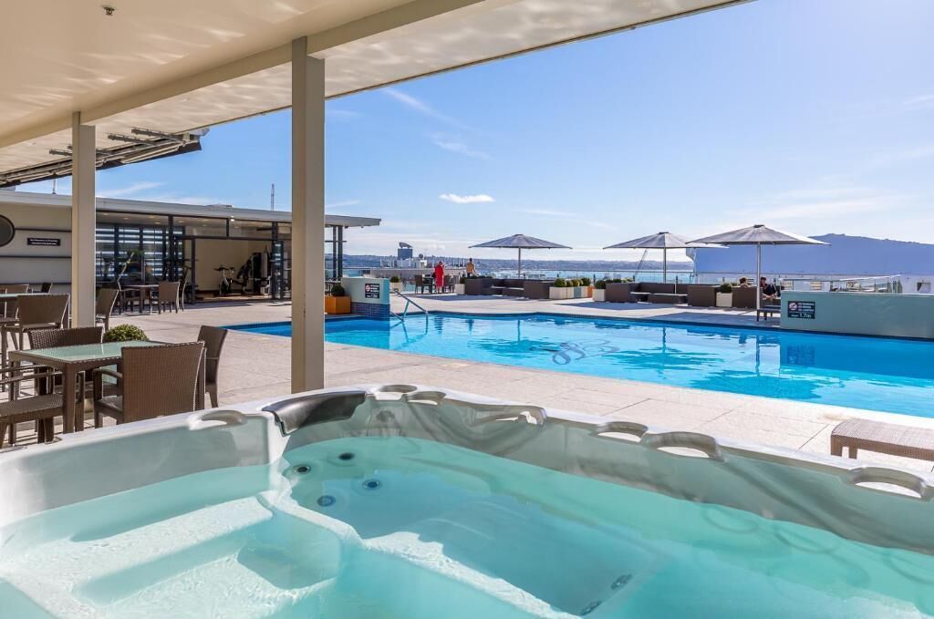 Un espace piscine comprenant un jacuzzi, des chaises longues et des parasols.