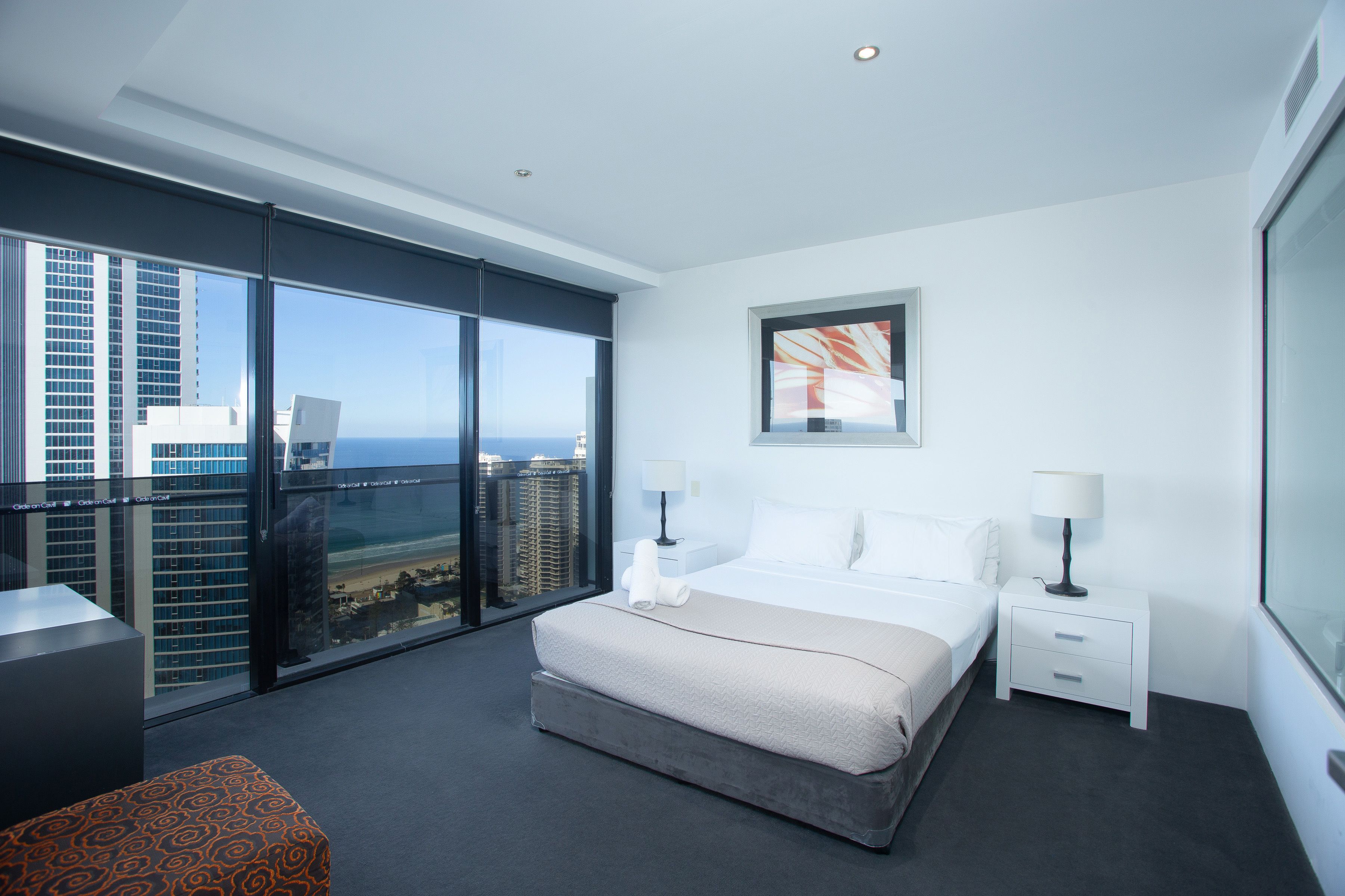 Een moderne hotelkamer met een groot bed, twee nachtkastjes, uitzicht op de stad en een groot raam.