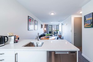 Une cuisine moderne dotée d’un îlot central, d’un lave-vaisselle encastré et donnant sur un espace de vie comprenant un canapé et une table.