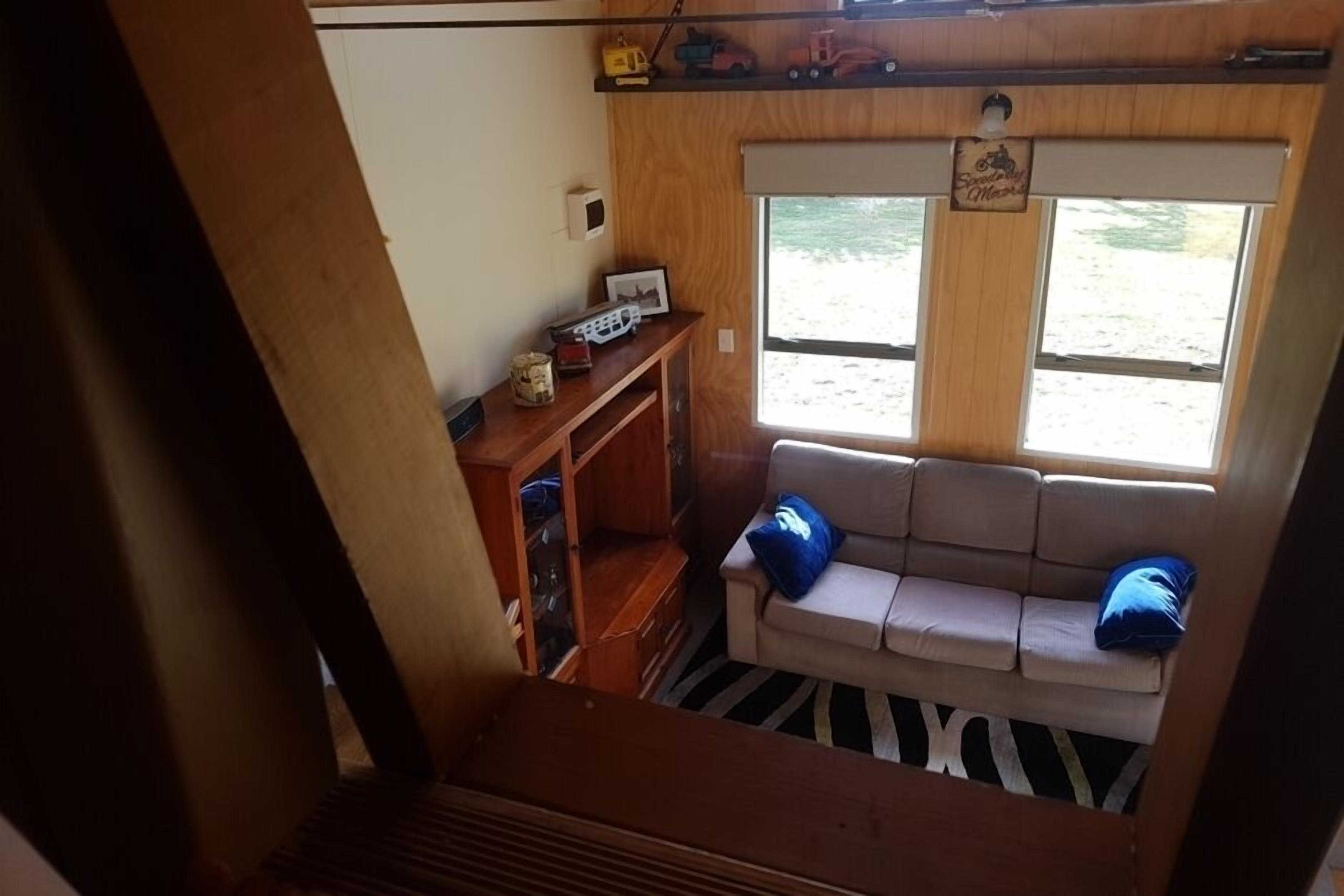 A cozy RV interior with a sofa, a small wooden shelf with toys, and a window offering a view of the outdoors.