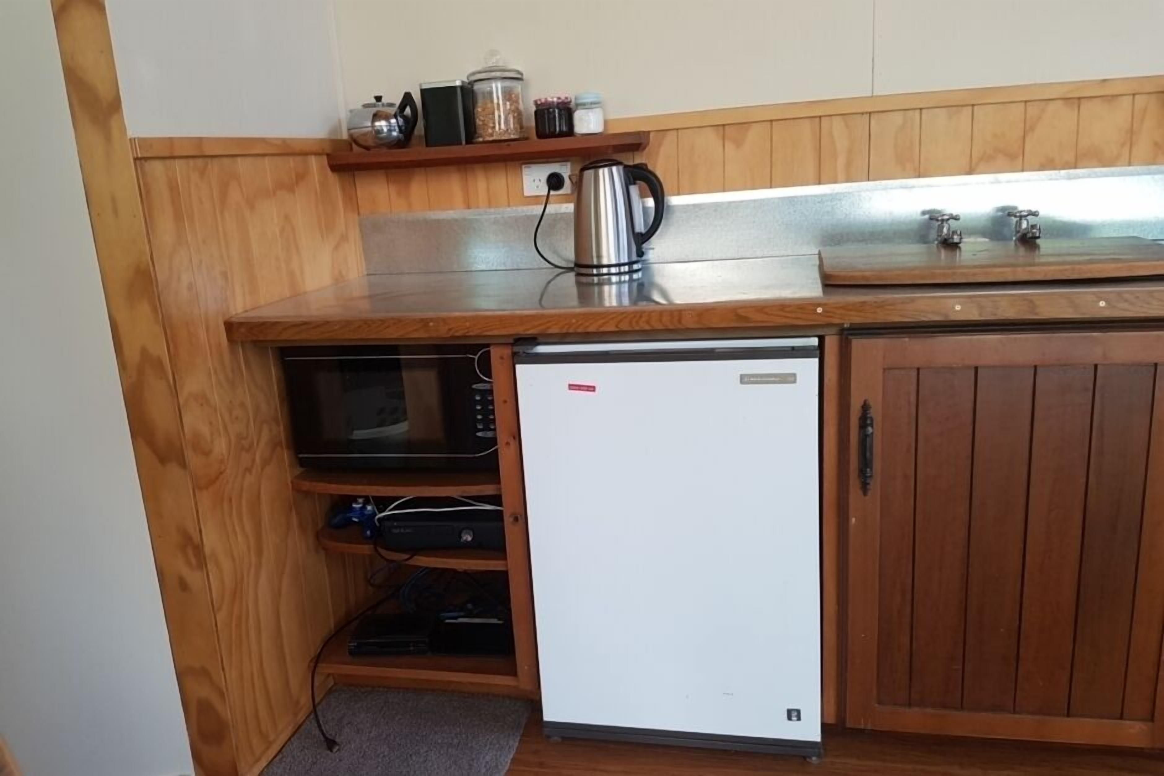 Eine kompakte Küche mit Mikrowelle, kleinem Kühlschrank und Holzschränken.