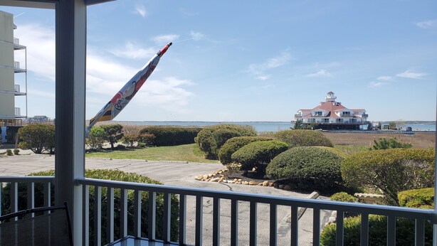 Un balcon donnant sur une grande maison située au bord de l’eau, une pelouse et un ciel dégagé.