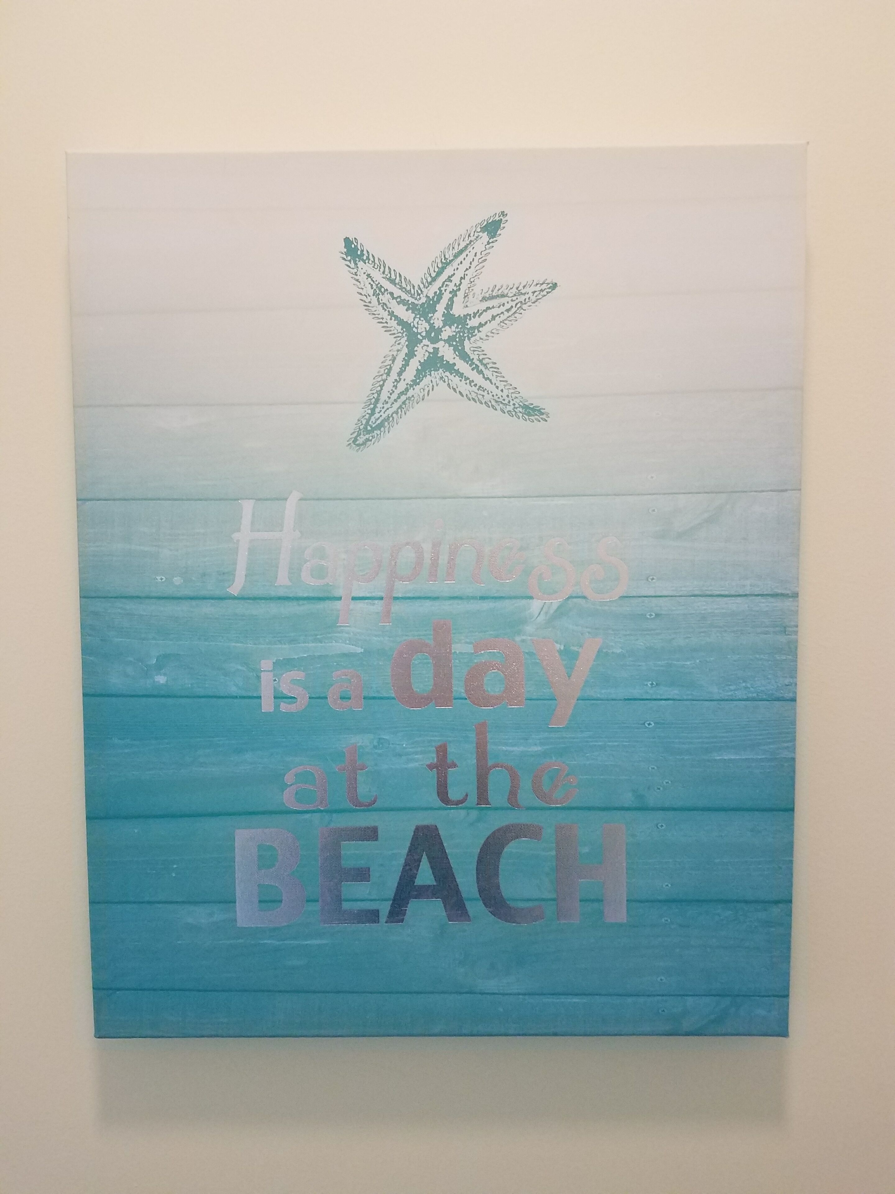 A wall hanging with a beach theme, featuring a starfish and the text "Happiness is a day at the beach."