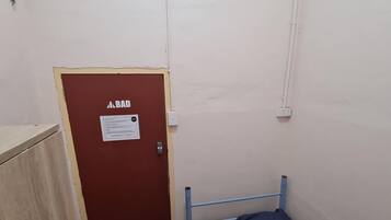 A small, narrow room with a single bed, a wooden cabinet, and a door labeled "BAD".