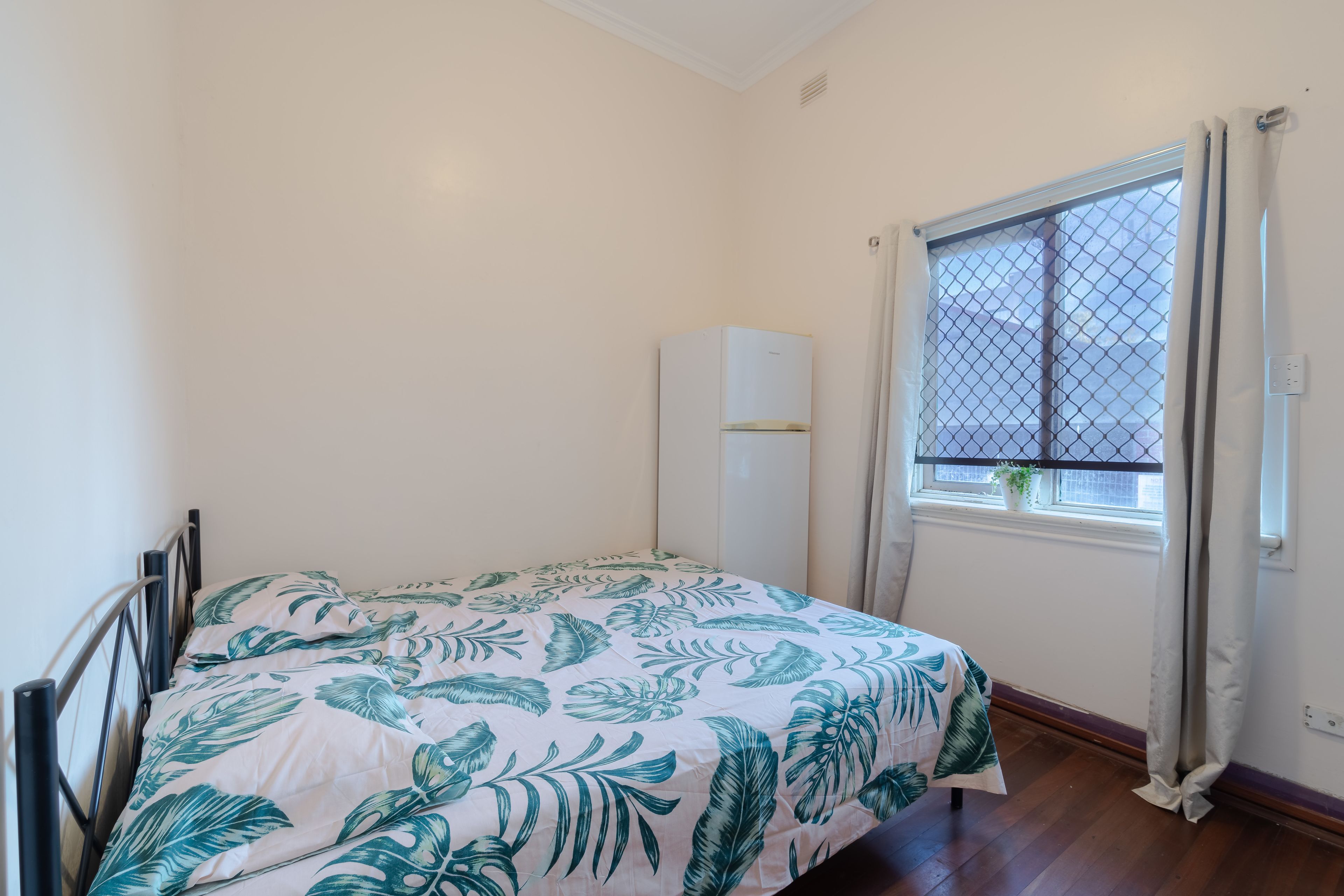 A small bedroom with a bed, a window with curtains, a radiator, and a wall-mounted air conditioner.