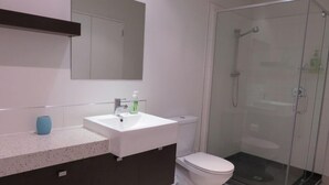 A modern bathroom with a white sink, dark cabinets, a toilet, and a glass-enclosed shower.