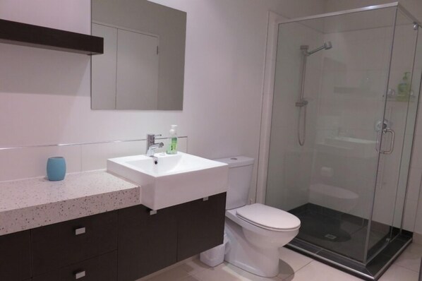 Ein modernes Badezimmer mit einem weißen Waschbecken, dunklen Schränken, einer Toilette und einer Duschkabine aus Glas.