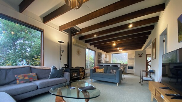 A modern living room with a glass coffee table, sofas, a fireplace, and a kitchen area visible through an open doorway.