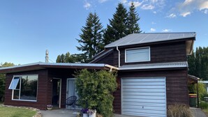 A two-story wooden house with a garage, a covered porch, and a small garden with potted plants.