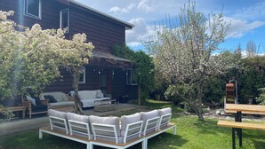 A wooden house with a porch, a white outdoor seating area, and flowering trees.
