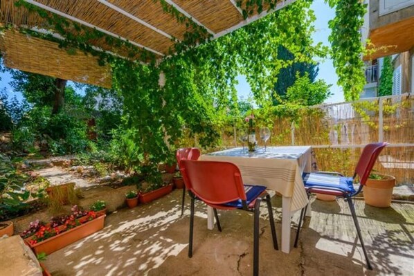 En udendørs patio med et bord og stole, omgivet af krukker med planter og en pergola med espalier.